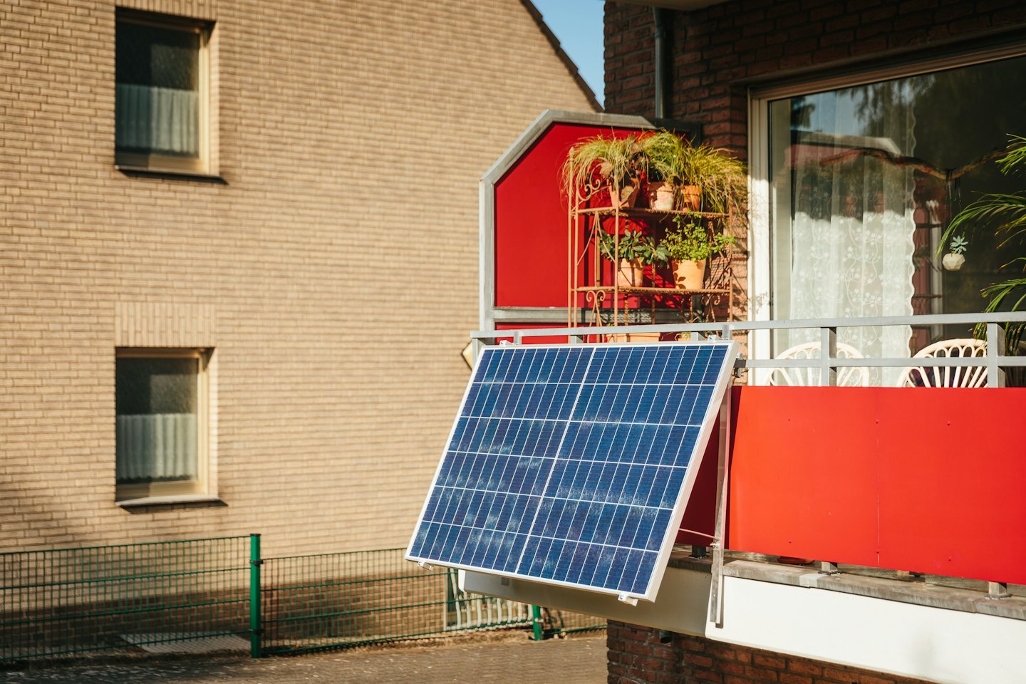 Solpanel på en röd balkongräcke med krukväxter.