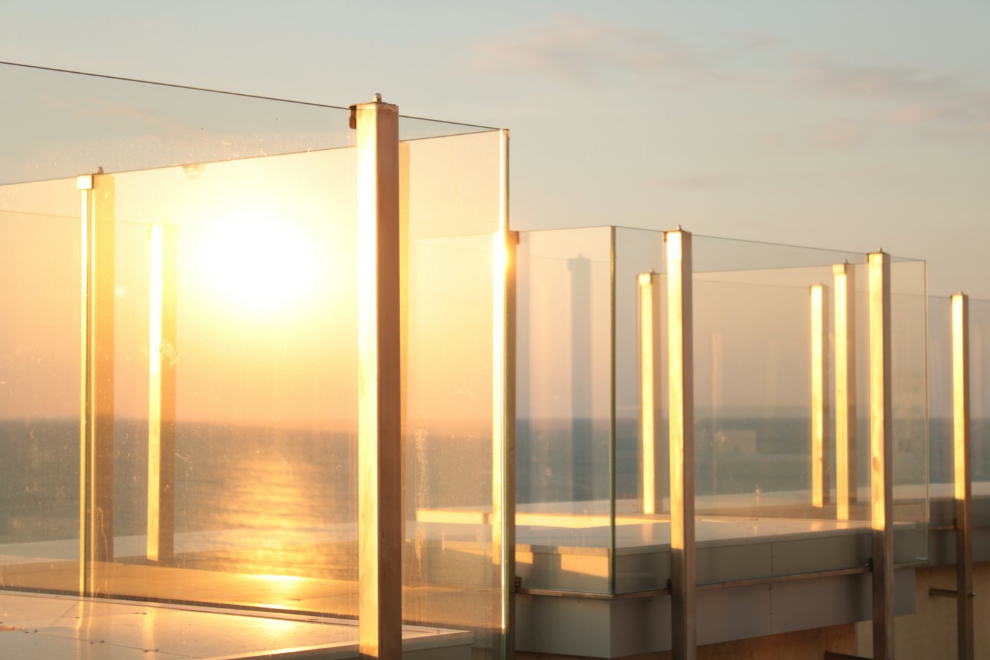 Modern balkongräcke i glas med utsikt över havet vid solnedgången.